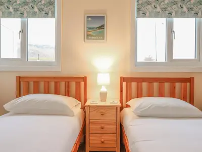two beds in a bedroom with two windows at 48 Glan Y Mor in Fairbourne