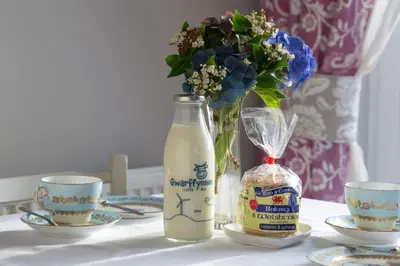a bottle of milk and two cups and a vase with flowers at Goitre Bach Cottage in Aberaeron