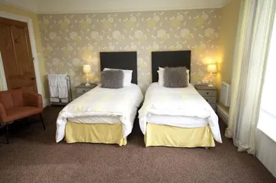 a bedroom with two beds and a chair at Leahurst Bed and Breakfast in Tywyn