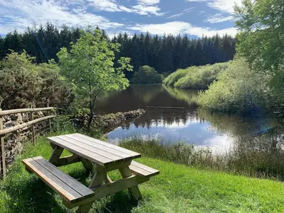 a wooden picnic table sitting next to a lake at The Barn at Pentregaer Ucha, with tennis court and lake in Oswestry
