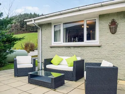 a patio with two wicker chairs and a table at Rhiw Gam in Abbey-Cwmhir