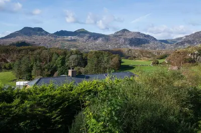 a house in a field with mountains in the background at Homely cottage with garden and mountain-view in Blaenau-Ffestiniog