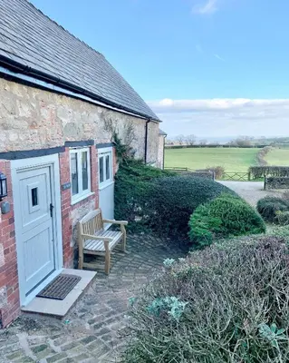 a brick house with a white door and a bench at The Stables at Pentregaer Ucha, tennis court & lake in Oswestry