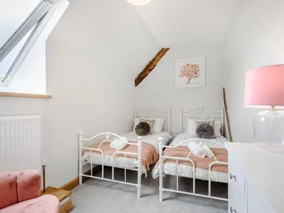 two beds in a white room with a pink lamp at Penshenkin Barn in Llanfihangel-nant-Melan