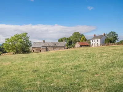 an open field with a house and buildings in the background at Gwrlodde in Talgarth