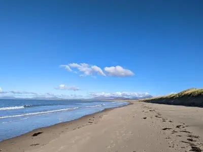 a beach with footprints in the sand and the ocean at Cosy, coastal cottage in Snowdonia in Harlech