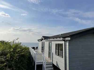 a white house with a chair on a deck at Sea Breeze Lodge in Aberaeron