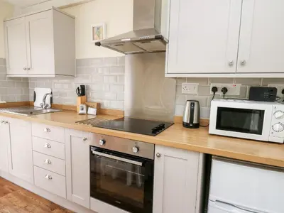 a kitchen with white cabinets and a wooden counter top at Honeysuckle Cottage in Llandrindod Wells