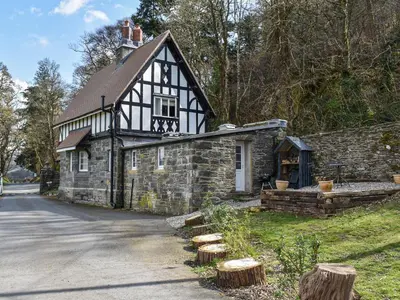 a black and white building with logs in front of it at Crogen Gatehouse Lodge in Corwen