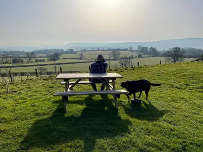 a person sitting on a bench with a dog at Pen Bryn Shepherd Hut in Hay-on-Wye