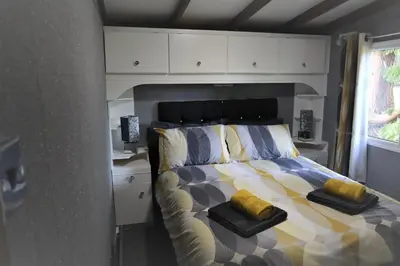 a bedroom with a bed with yellow pillows on it at HEDDFAN, Luxury 3 bedroom timber lodge, Now with WiFi, Caer Beris Holiday Park, Builth Wells, SORRY NO TRADESMEN OR CONTRACTORS ALLOWED in Builth Wells