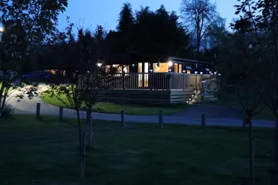 a house lit up at night with lights at HEDDFAN, Luxury 3 bedroom timber lodge, Now with WiFi, Caer Beris Holiday Park, Builth Wells, SORRY NO TRADESMEN OR CONTRACTORS ALLOWED in Builth Wells