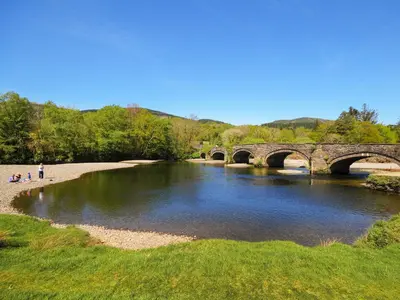 a bridge over a river with people walking on the shore at Bryn Araul in Rhydymain