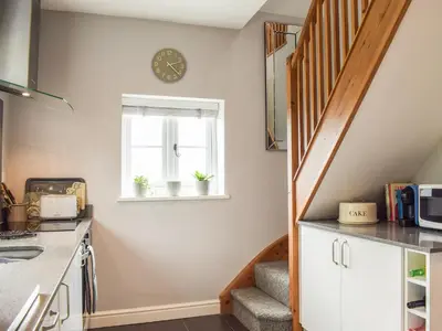 a kitchen with a staircase and a clock on the wall at Little Bank Cottage in Lane to Richards Castle