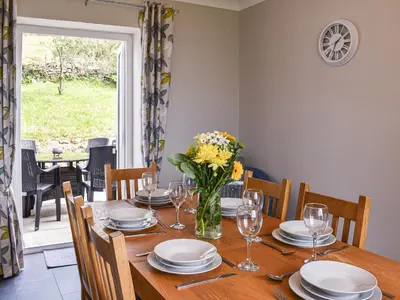 a dining room with a wooden table with a vase of flowers at Bryn Derwen in Harlech