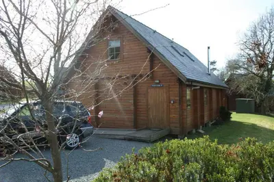 a wooden barn with a car parked in front of it at Luxury 3 bedroom, 3 bathroom lodge with hot tub in Llanbedr