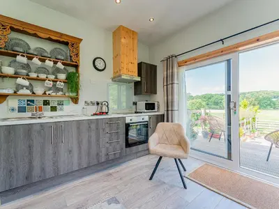 a kitchen with a chair in front of a sliding glass door at Cwtch Enrico - Uk39064 in Scyborycoed
