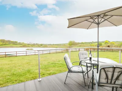 a patio with a table and chairs and an umbrella at Llyn Cae Ty Nant Fishery Holiday Let in Lampeter