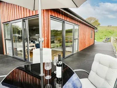 a house with a glass table and two chairs on a deck at Llyn Cae Ty Nant Fishery Holiday Let in Lampeter