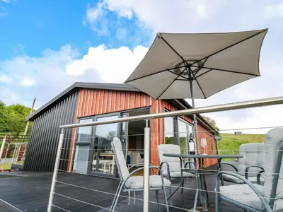 a patio with a table and chairs and an umbrella at Llyn Cae Ty Nant Fishery Holiday Let in Lampeter