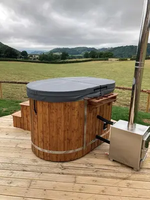 a hot tub on a wooden deck with a field at Delor - Bryntalch Glamping Pods in Montgomery