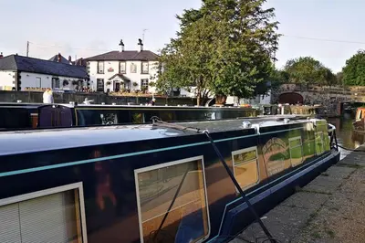 a boat is docked on a river with buildings in the background at Hillside Cottage, countryside views near Llangollen in Corwen