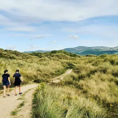 two people walking down a dirt path in a field at Spacious heated Yurt with Hot tub, 5 mins to beach in Bow Street