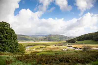 a river in a field with mountains in the background at Empress En Suite Wagon in Arthog