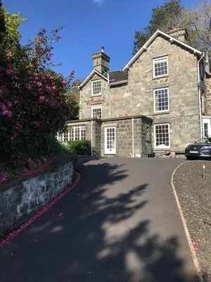 a large stone house with a car parked in the driveway at Bryn Mair Gardens in Dolgellau