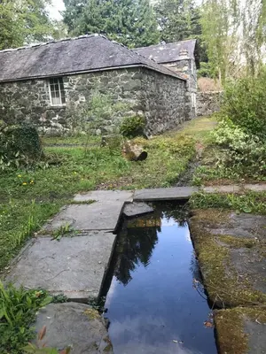 an old stone house with a pond in front of it at Bryn Mair Gardens in Dolgellau