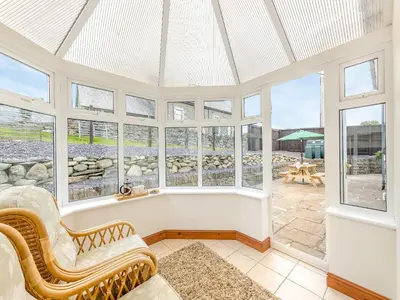 a conservatory with windows and chairs and a patio at Cysgod Y Capel in Cerrigydrudion
