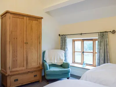 a bedroom with a blue chair and a cabinet at Colstey Farmhouse in Acton
