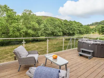 a deck with a hot tub and chairs and a table at The Cabin at Evelyns Retreat in Corwen