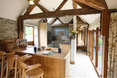 a kitchen with wooden ceilings and a large island with chairs at Garden Cottage at Eaton Manor in Eaton