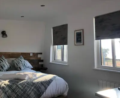 a bedroom with a bed and two windows at MAESLLAN CABINS - 'Golwg Y Mor' in Cross Inn
