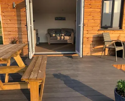 a wooden deck with a couch and a wooden table at MAESLLAN CABINS - 'Golwg Y Mor' in Cross Inn