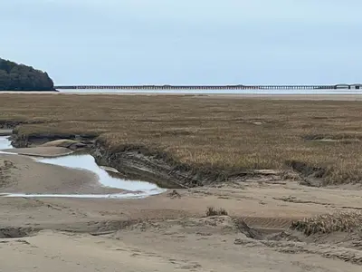 an empty beach with a bridge in the distance at Harbour Apartment in Barmouth
