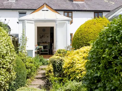 a white house with a pathway leading to the front door at Cosy cottage with views over the Shropshire hills - Pass the Keys in Ludlow