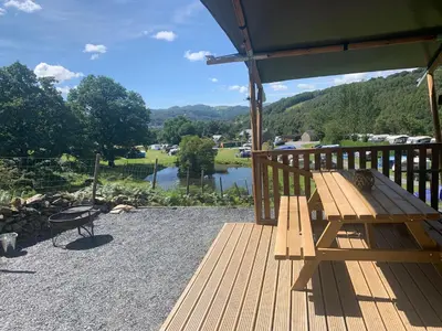 a wooden bench on a deck with a view of a lake at Mountain View Safari Tent with Hot Tub in The Heart of Snowdonia in Dolgellau