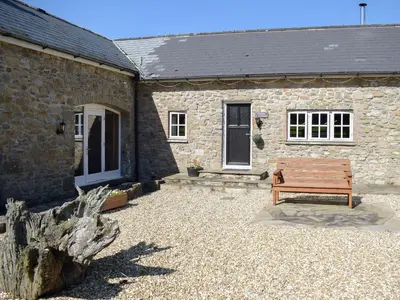 a wooden bench sitting outside of a stone building at Dairy Cottage in Talley