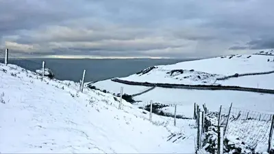 a snow covered hill with a fence and a body of water at Yr Hen Beudy in Tywyn