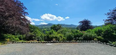 a garden with a stone wall and trees and mountains at Cader en suite at Pen Y Coed Hall exclusive Luxury Hot Tub in Dolgellau