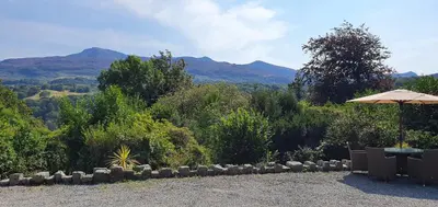a patio with an umbrella and mountains in the background at Cader en suite at Pen Y Coed Hall exclusive Luxury Hot Tub in Dolgellau