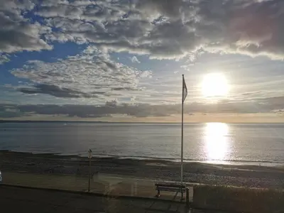 a bench on the beach with the sun in the sky at Lovely Seafront 2 bed flat in Aberystwyth in Aberystwyth