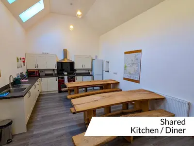 a kitchen with two wooden tables and a kitchen at Cwm Clyd Longhouse in Llanwrthwl