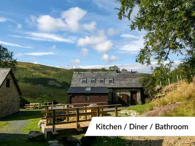 a barn with a wooden bridge in front of a house at Cwm Clyd Longhouse in Llanwrthwl
