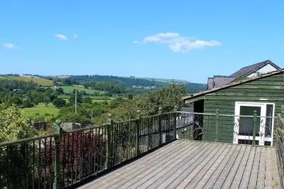 a wooden deck with a house on a hill at Redwood Lodge, Dee Valley Stays - cosy microlodge with detached private shower & WC in Corwen
