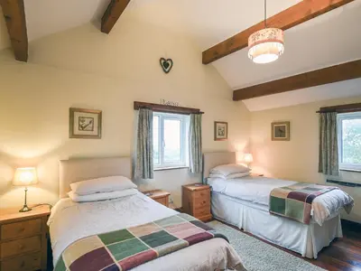 two beds in a room with two windows at Heron Cottage in Bishops Castle
