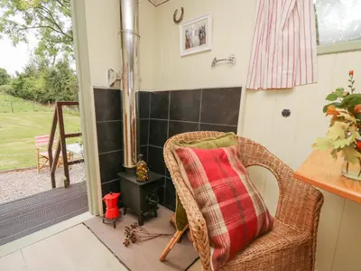 a wicker chair with a red pillow sitting next to a door at Tilly Gypsy-style Caravan Hut in Brecon