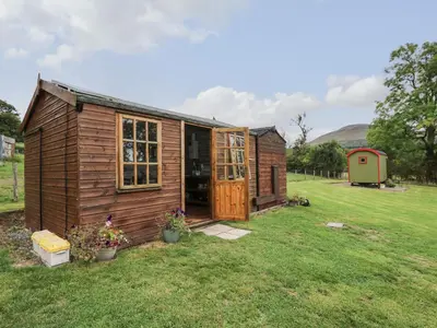 a small wooden shed in a grass field at Tilly Gypsy-style Caravan Hut in Brecon